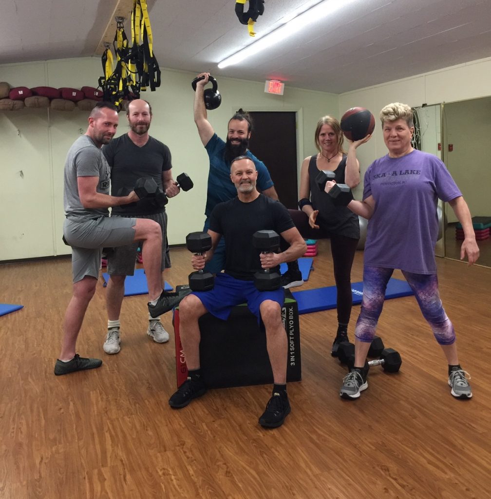 Members of a group fitness class, holding weights, crowd around James Chicalo