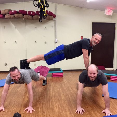 James Chicalo, fitness trainer, does a plank, on the backs of two of his fitness clients, in a gymnasium in Okanagan Falls.