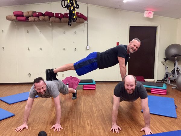 James Chicalo, fitness trainer, does a plank, on the backs of two of his fitness clients, in a gymnasium in Okanagan Falls.